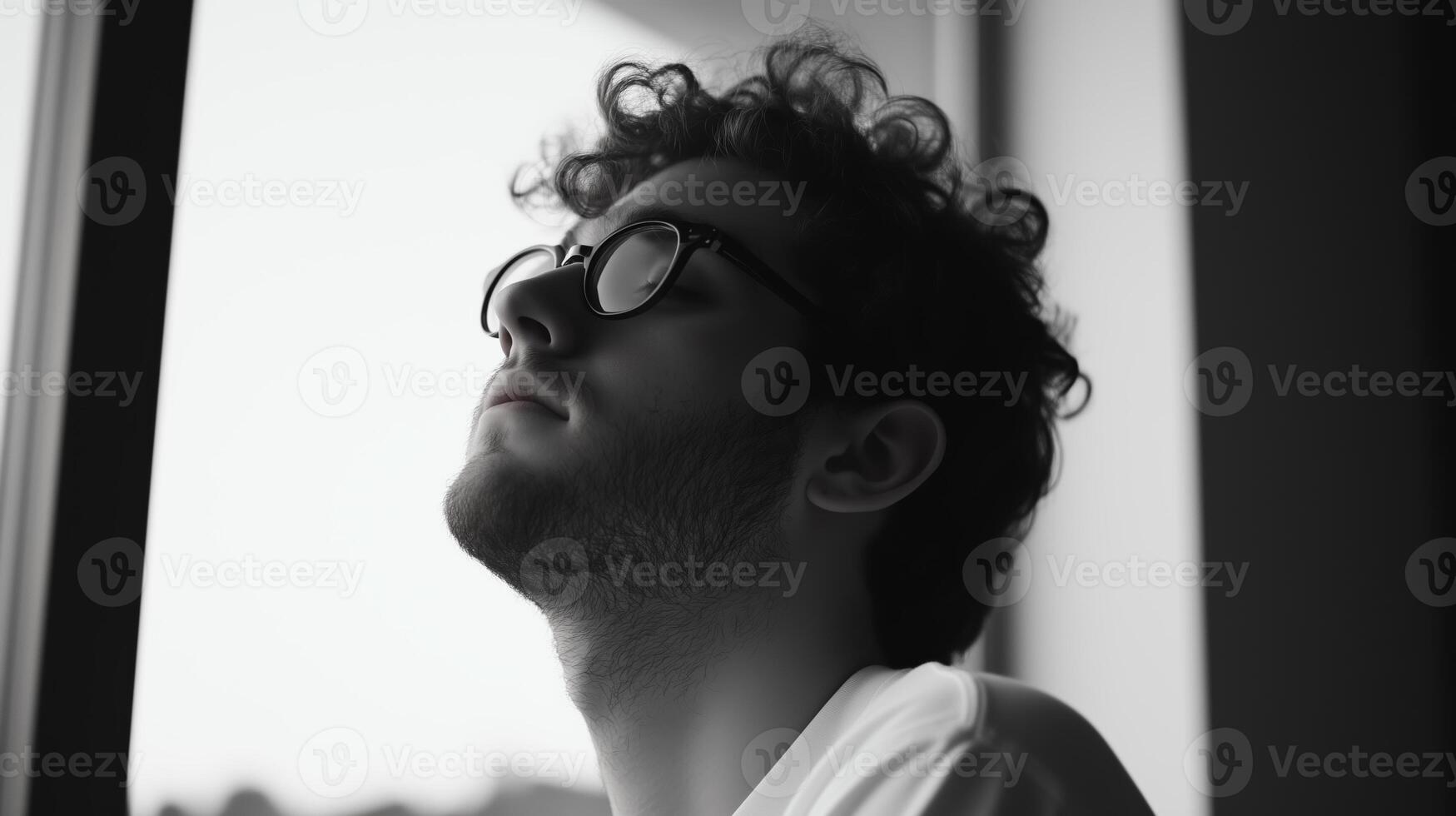 A young man with curly hair gazes thoughtfully out a window on a cloudy day, reflecting on personal moments and aspirations photo
