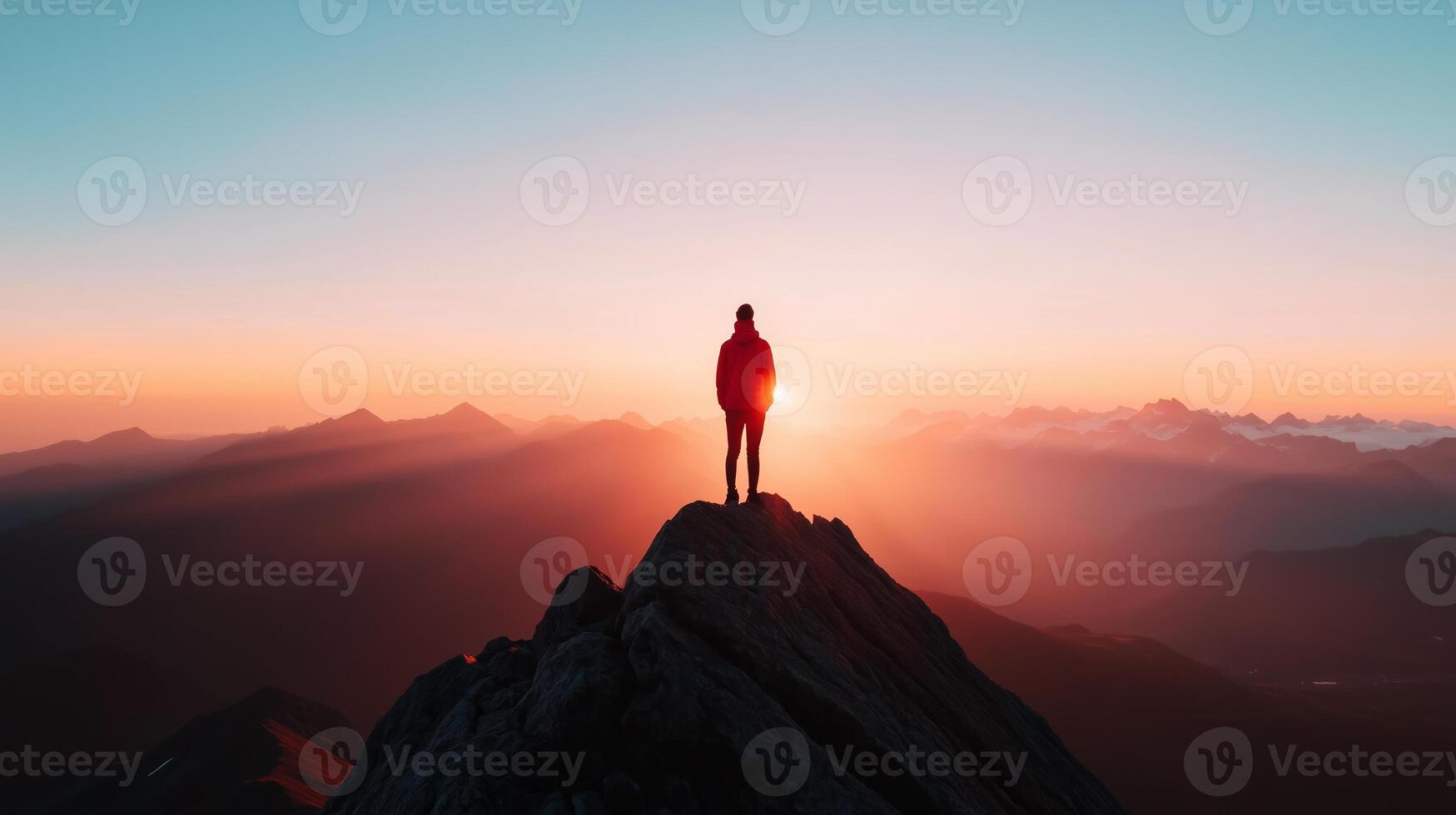 A lone traveler stands atop a mountain peak at sunset, surrounded by breathtaking landscapes and colorful skies photo
