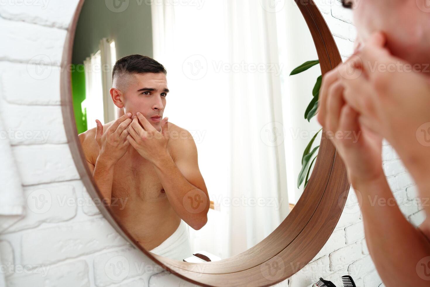 Young man looking in the mirror in the bathroom preparing for the day photo