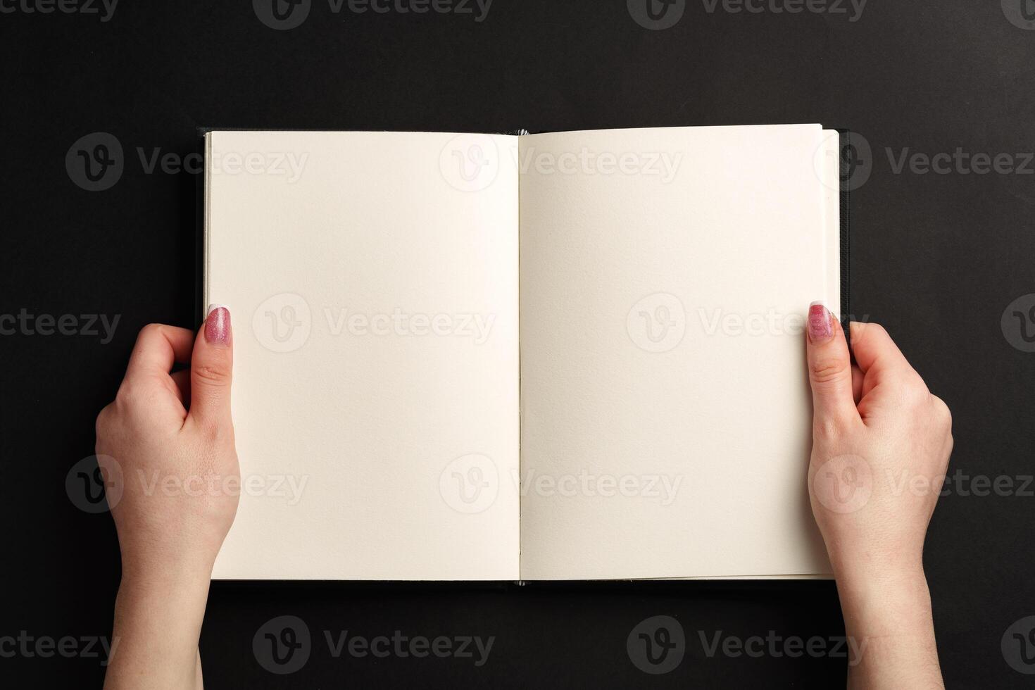 Open notepad in hands on black background photo