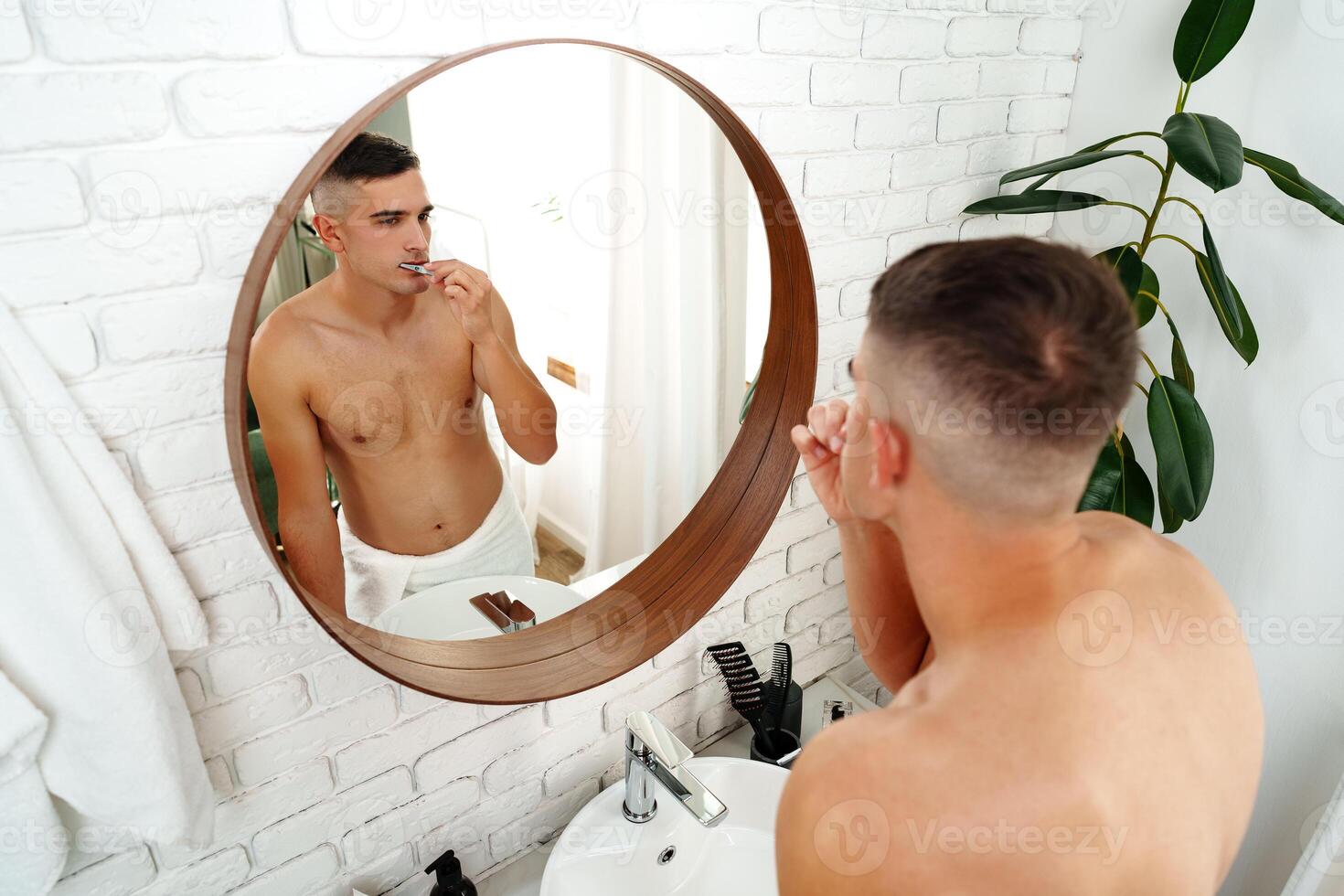 Young man brushing teeth against the mirror in the bathroom photo