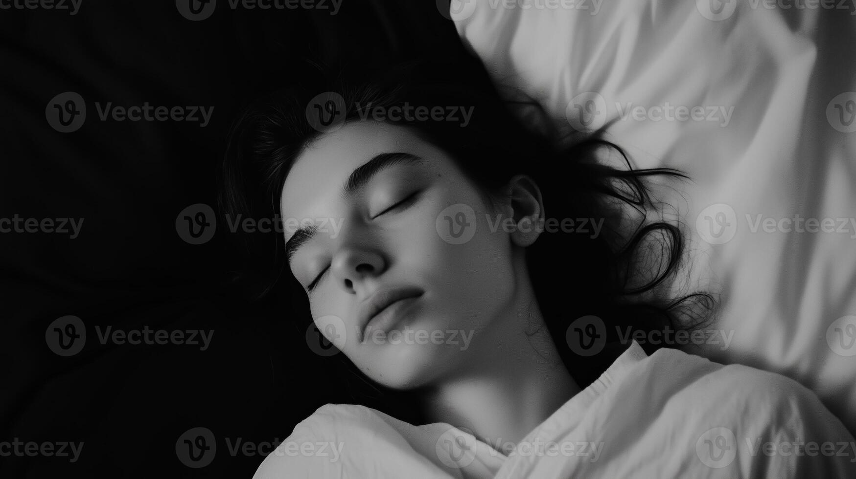 A young woman resting peacefully on a bed with soft pillows, captured in serene black and white tones during the night photo