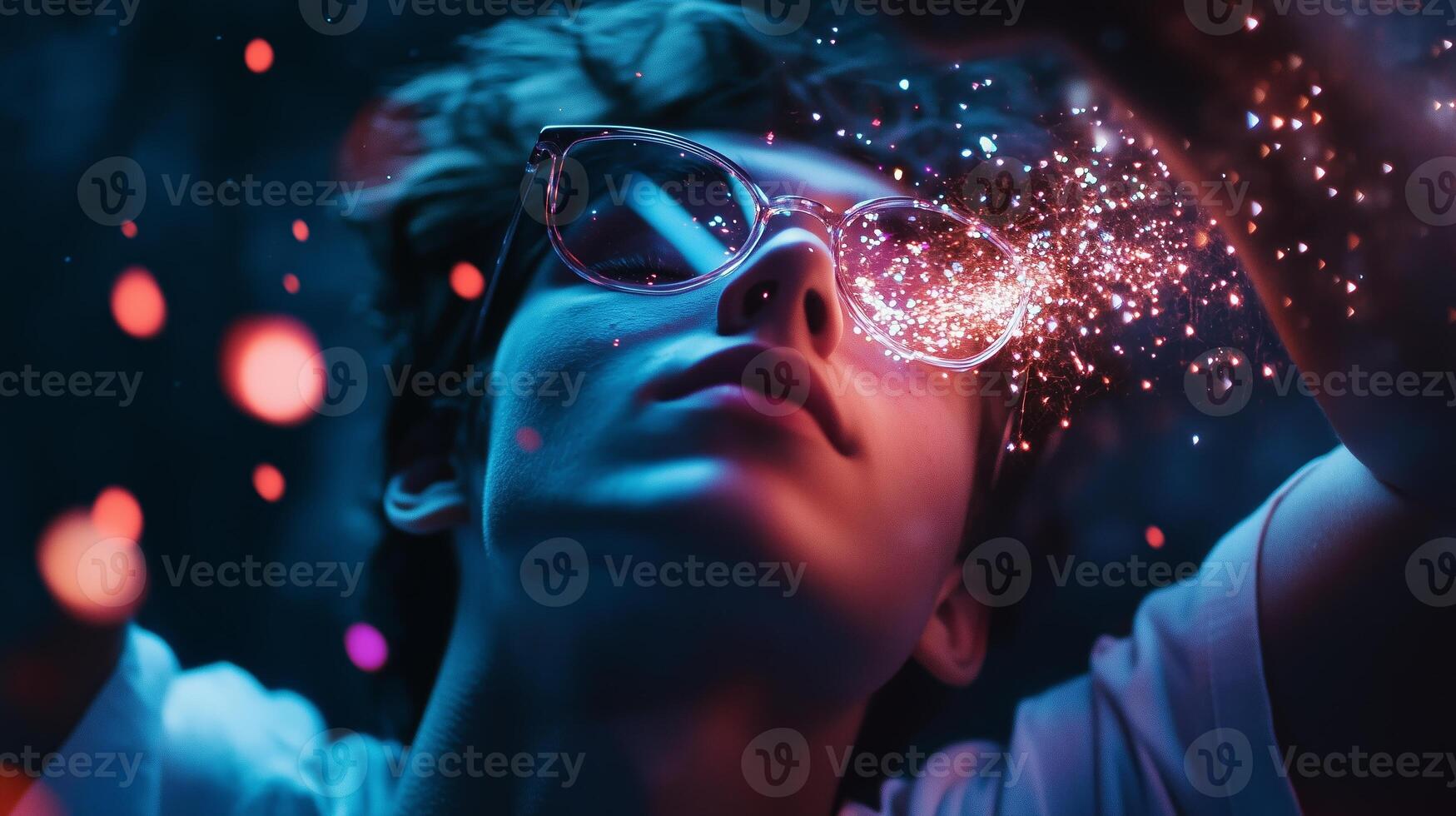 A young person wearing stylish glasses interacts with vibrant light particles in a creative, dreamlike setting at dusk photo