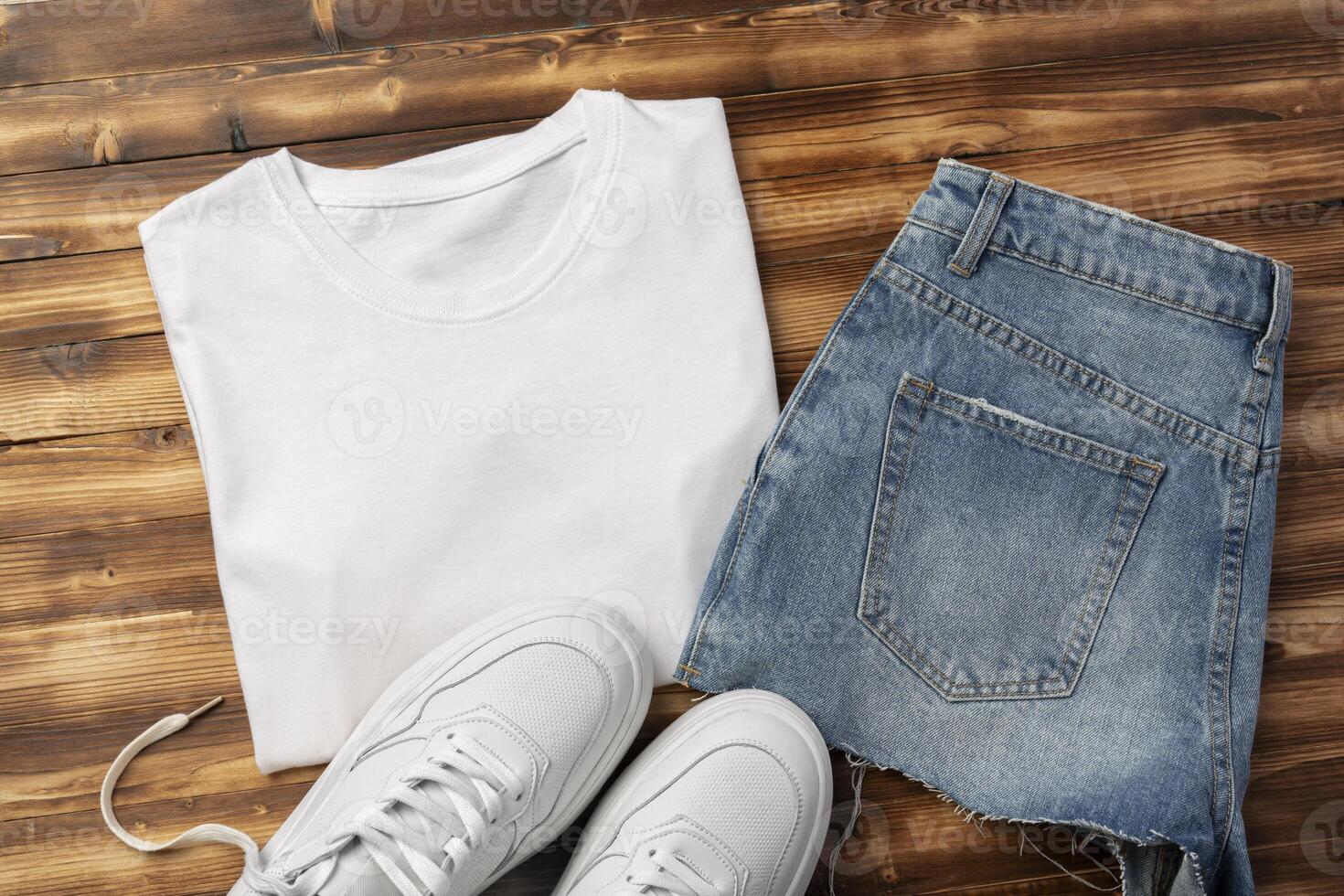 Cotton T-shirt, jeans and sneakers on wooden background top view photo