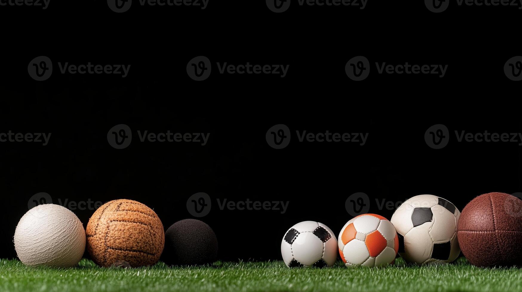A collection of various sports balls arranged neatly on green grass against a dark background photo