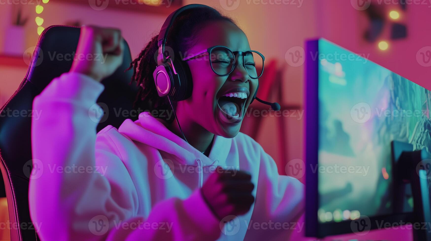 Excited gamer celebrating a victory while wearing headphones at her colorful gaming setup in the evening photo