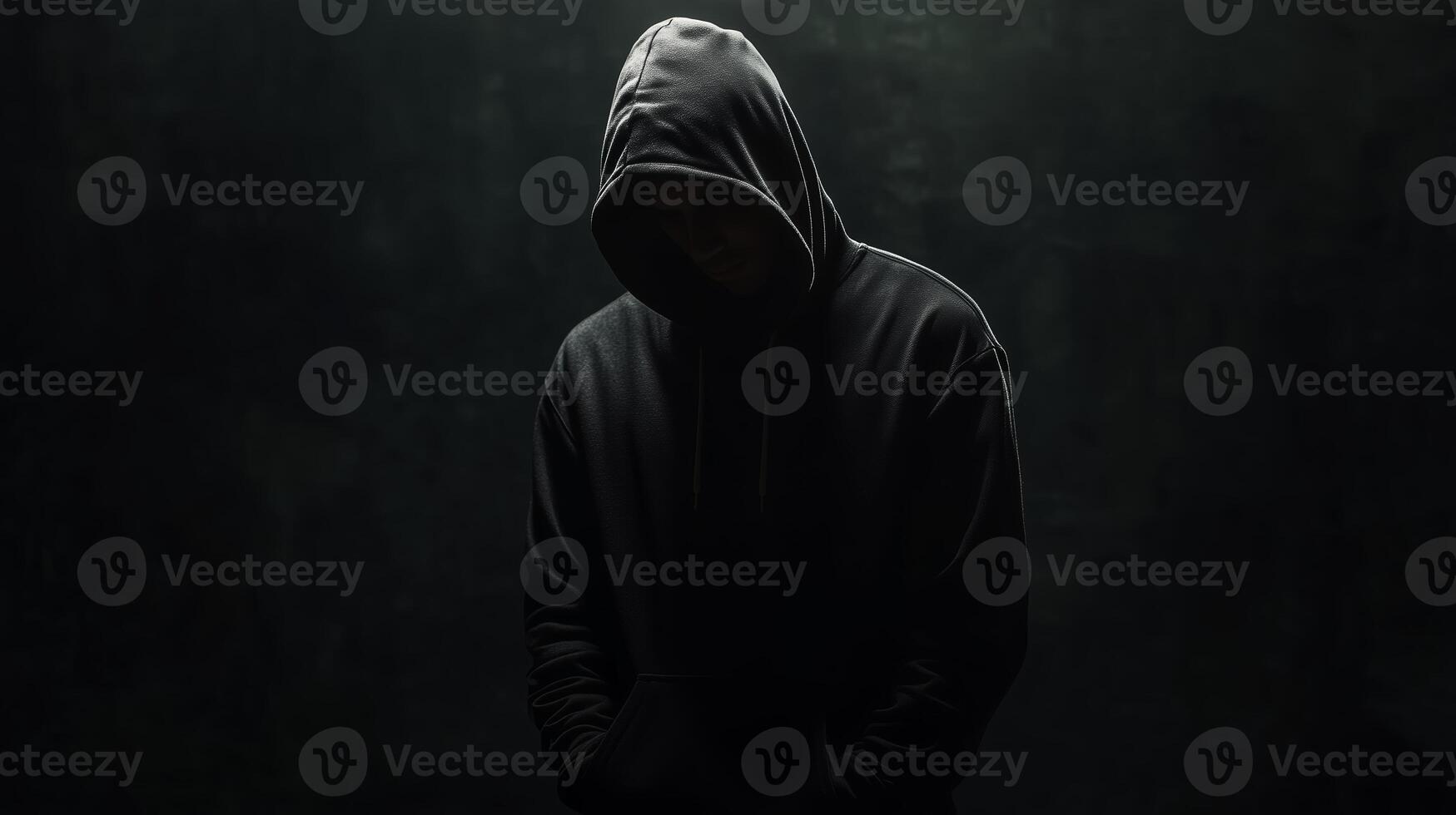 A solitary figure in a dark hoodie stands quietly against a shadowy backdrop, evoking a sense of mystery and introspection in a low-lit environment photo
