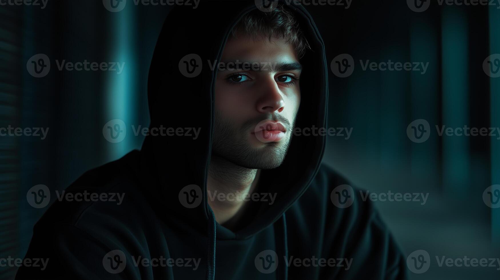 A young man wearing a hooded sweatshirt gazes thoughtfully into the distance in a dimly lit urban setting during the evening photo