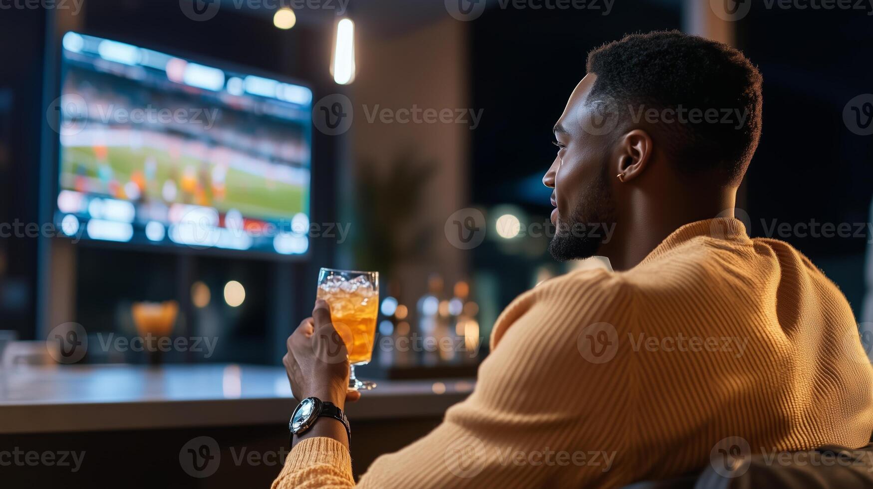 A man enjoys a drink while watching a sports game on a large screen in a modern lounge during the evening photo