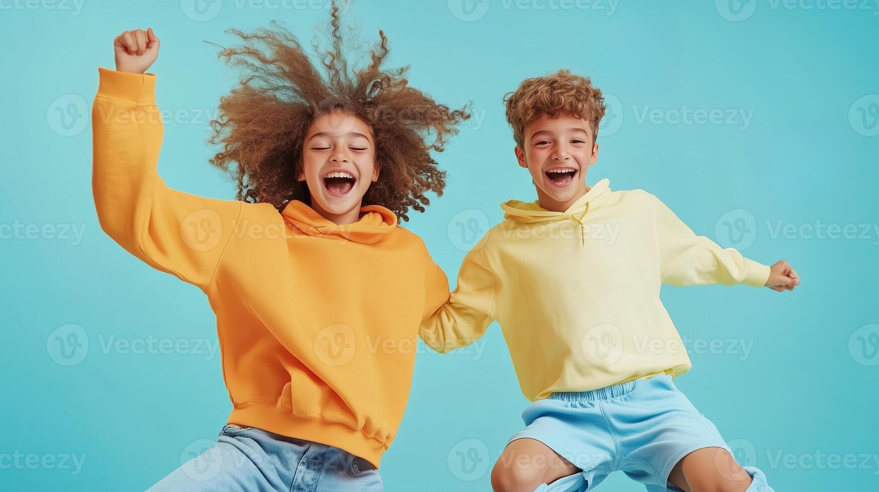 Two children joyfully jumping in colorful hoodies against a bright blue background on a sunny day photo