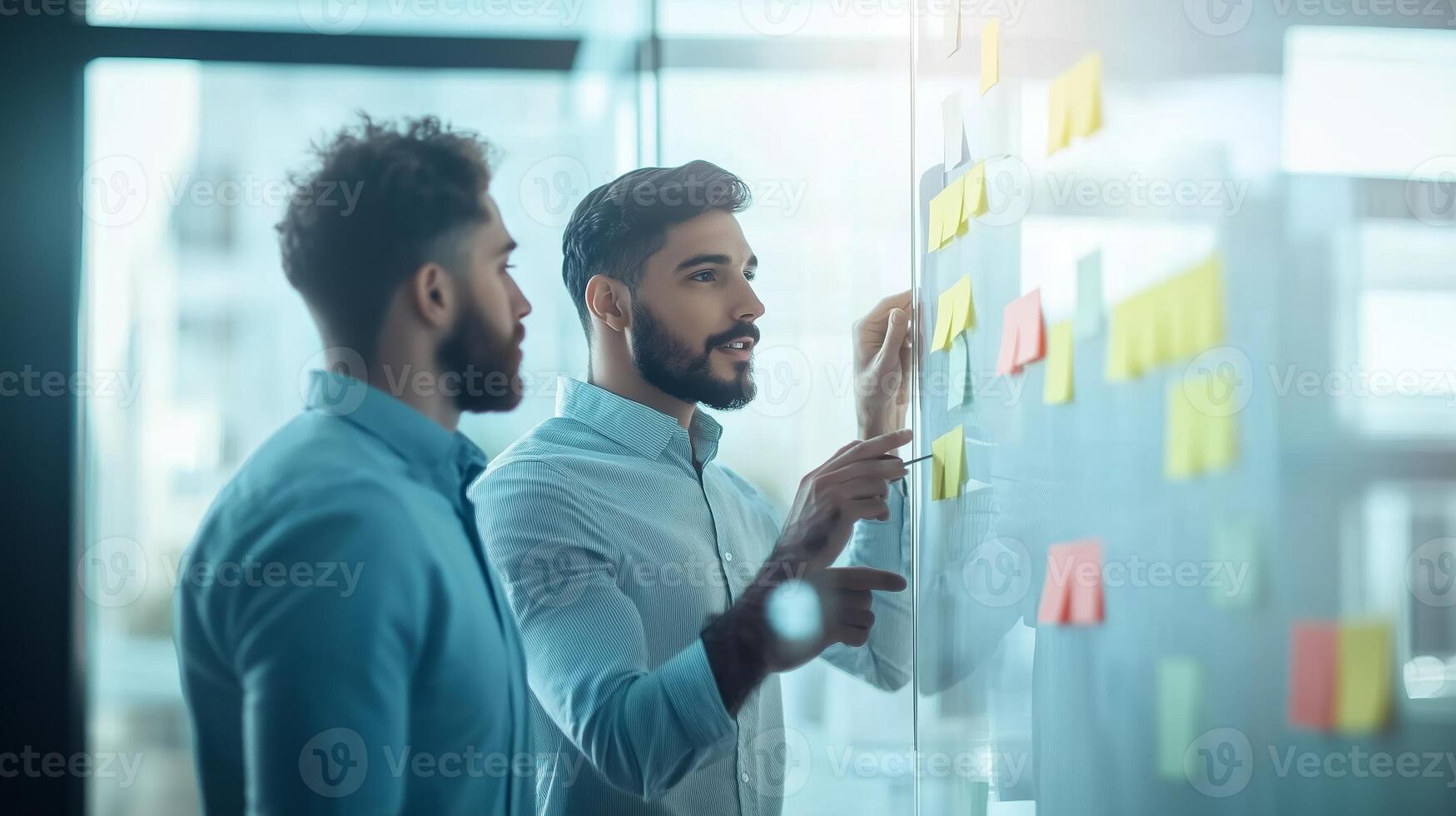 Two professionals brainstorming ideas on a glass wall in a modern office setting during the daytime photo