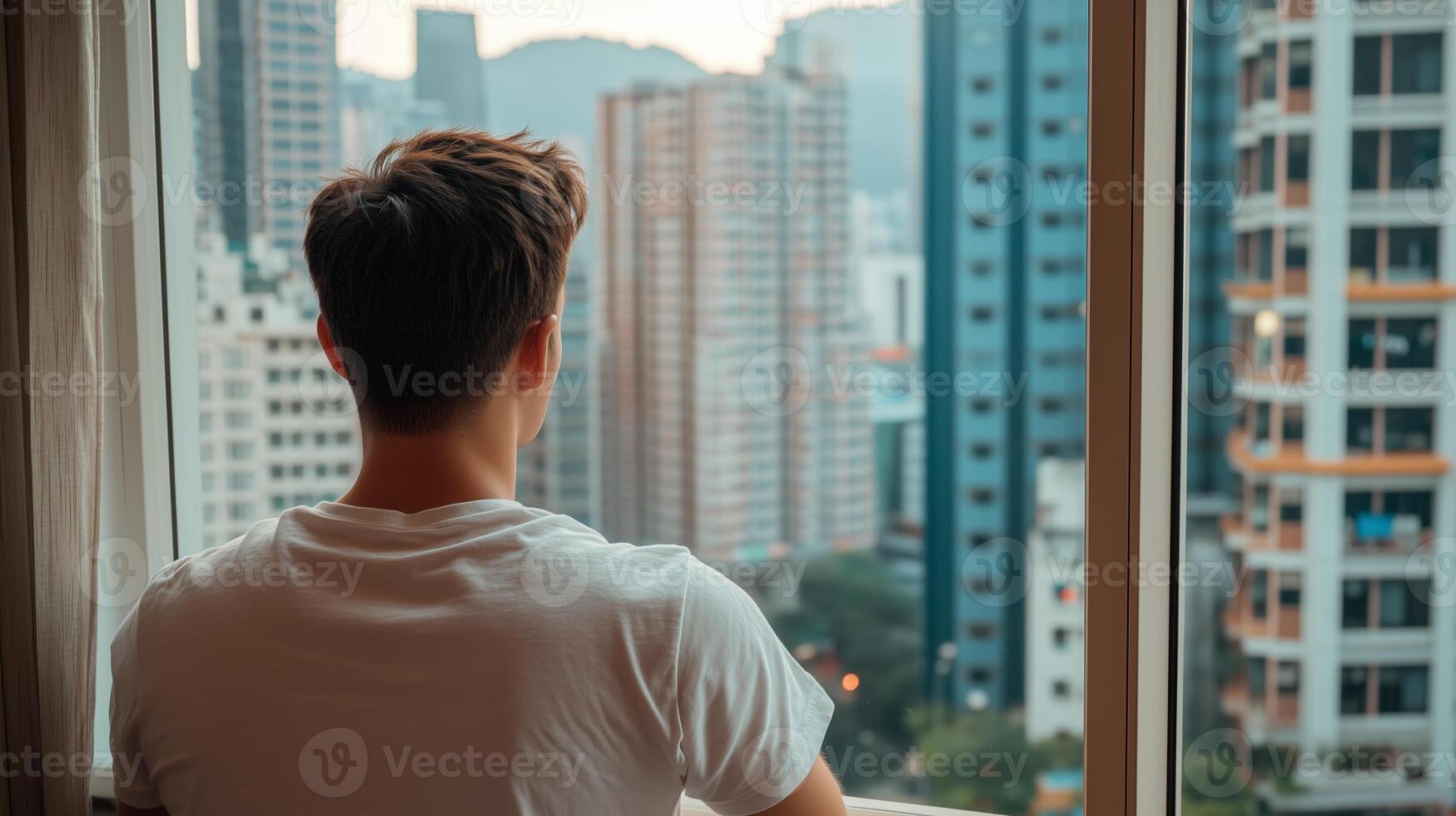 A man gazing out at a bustling city skyline from his apartment window in the late afternoon light photo