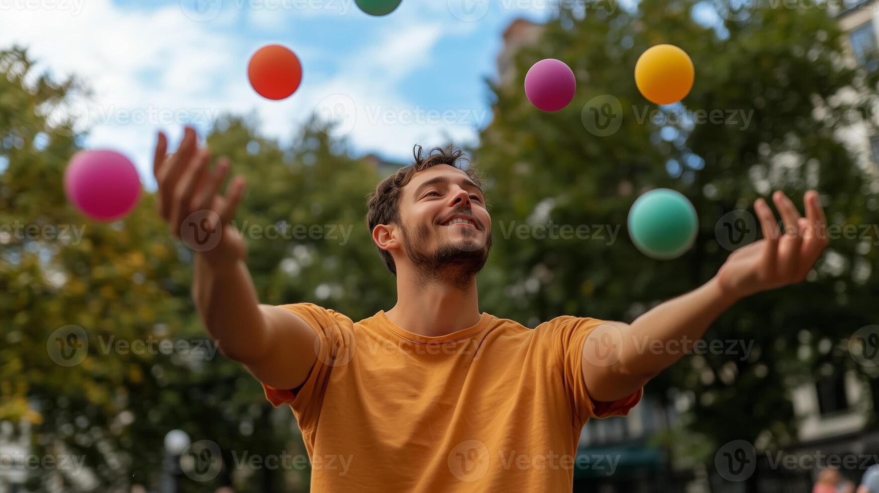 A man joyfully juggling colorful balls in a park filled with trees and a bright sky during a sunny afternoon photo