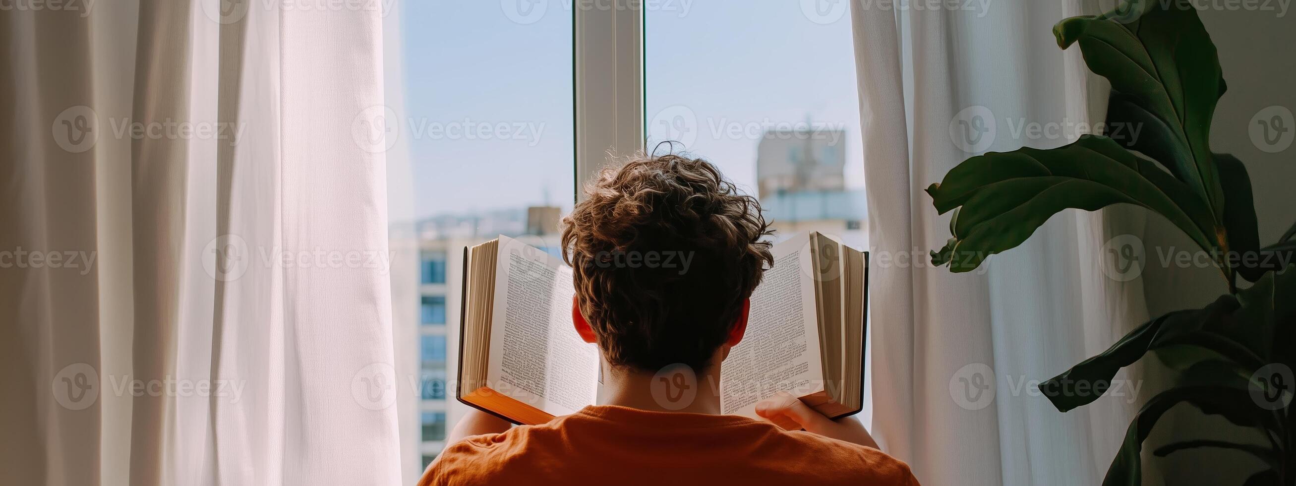 A person enjoys reading a book by the window while gazing at the city skyline during a sunny day photo