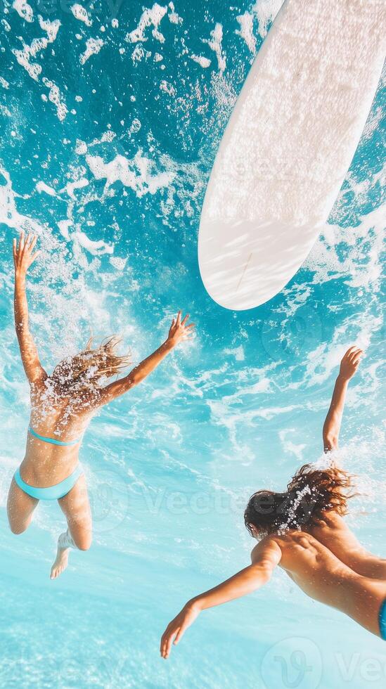 Two surfers diving into clear ocean water beneath a bright sunlit sky in a vibrant tropical setting photo