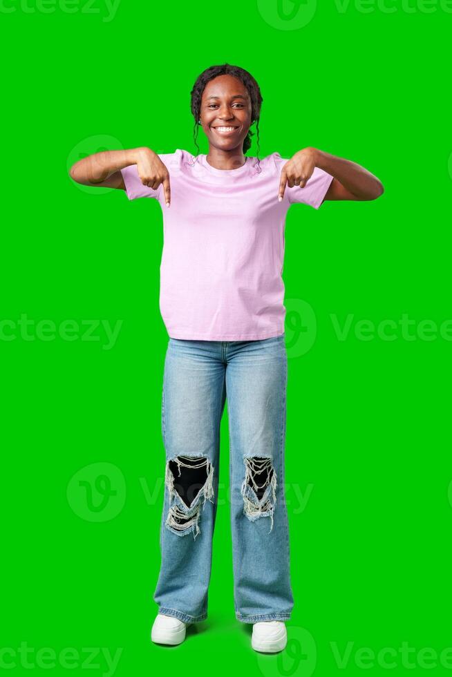 Smiling young woman pointing downwards against a bright green background photo