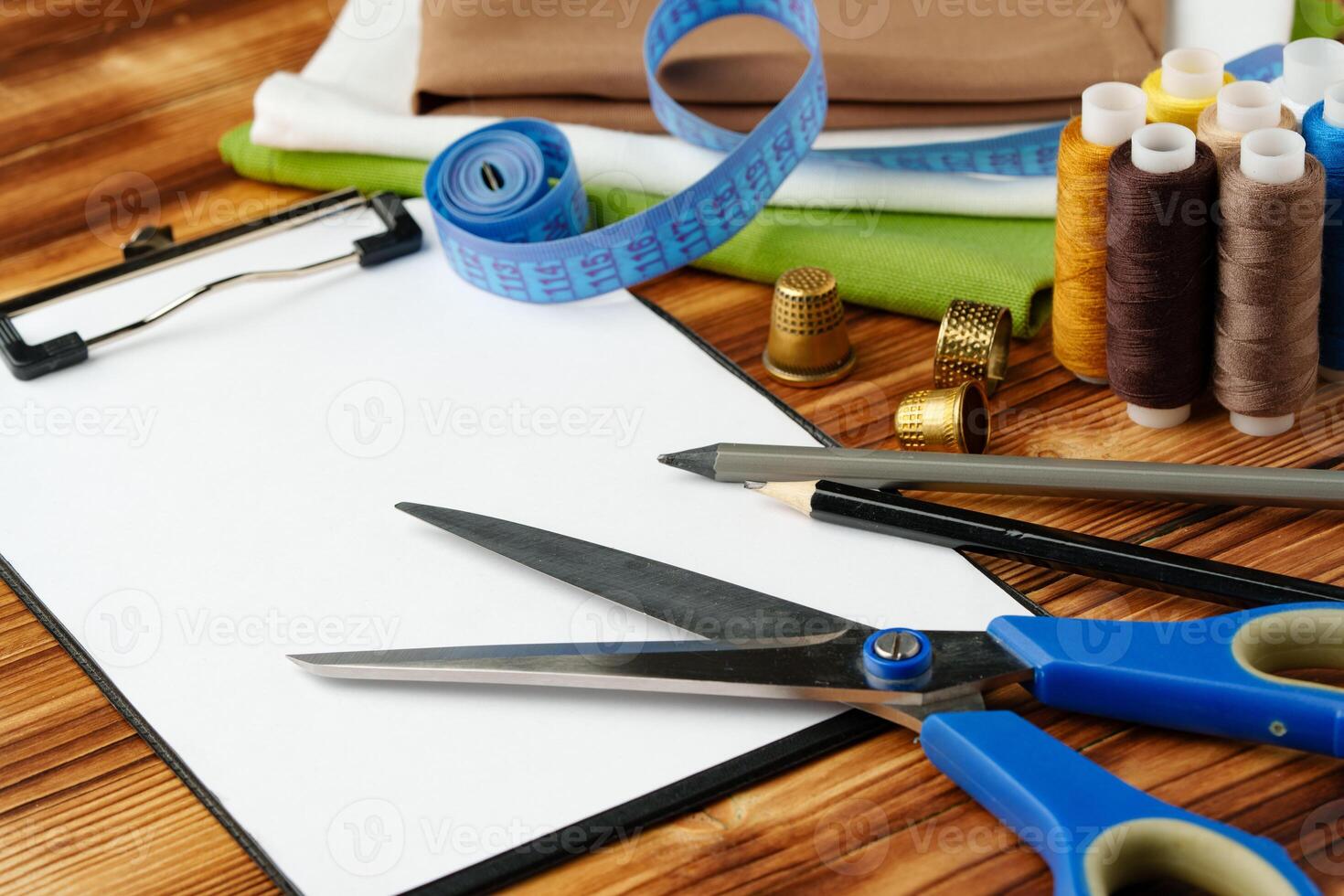 Colorful sewing supplies arranged around a blank clipboard on a wooden table photo