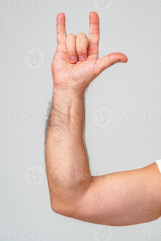 A person makes a hand gesture with the pinky and index finger raised against a plain background photo