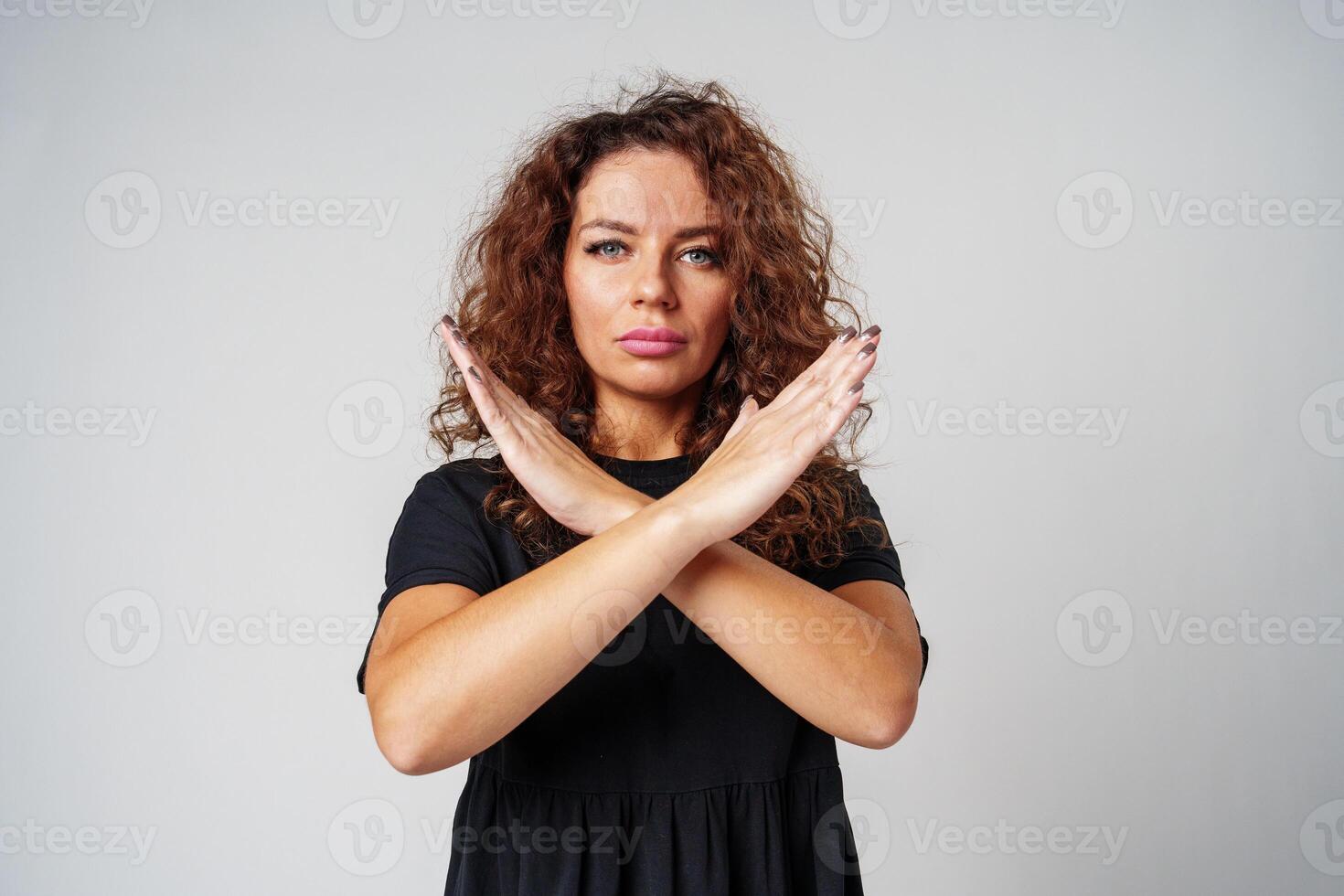 Woman in a black dress standing against a gray background with arms crossed photo