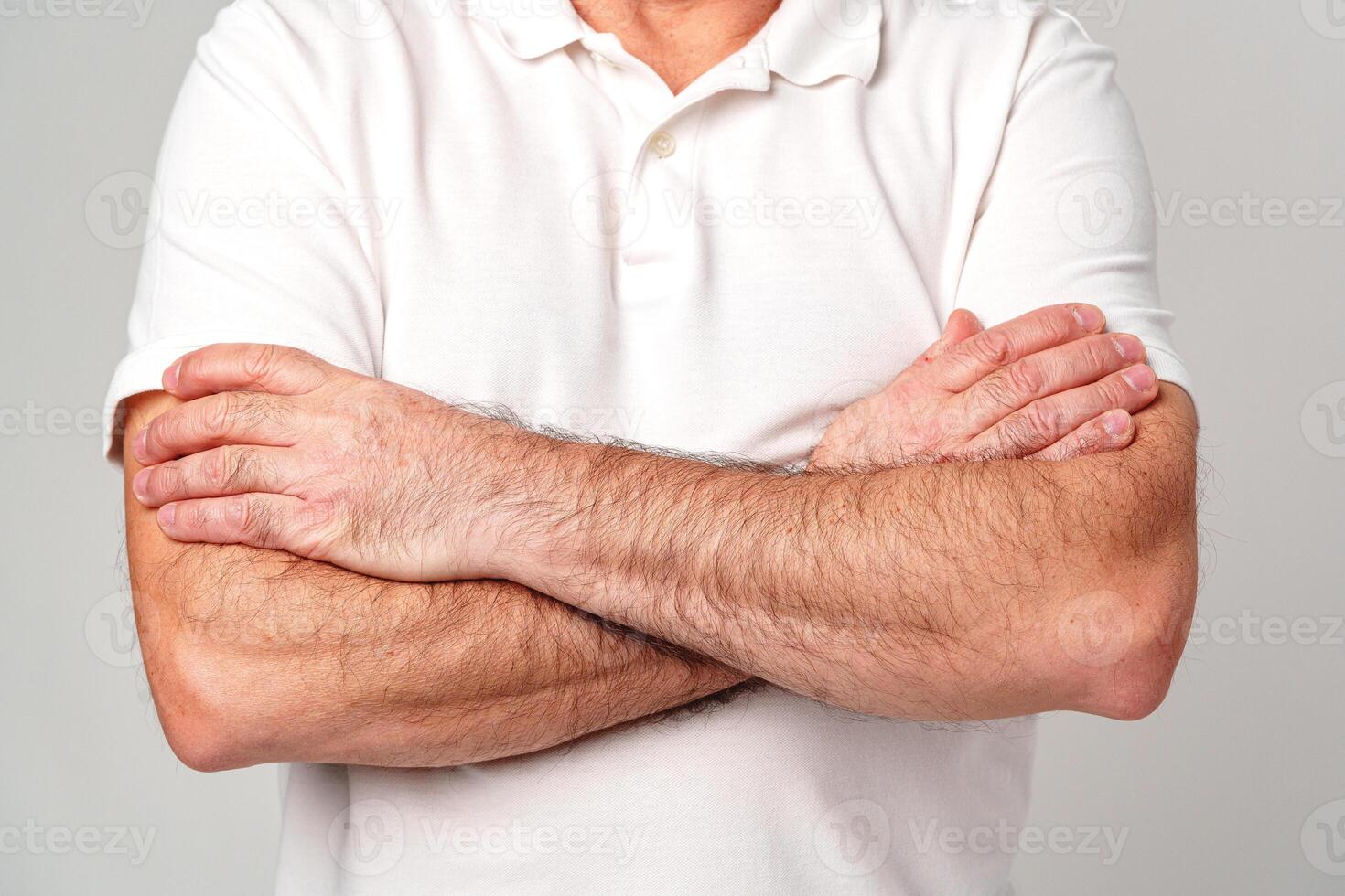 A man with crossed arms wearing a white polo shirt stands against a neutral background photo