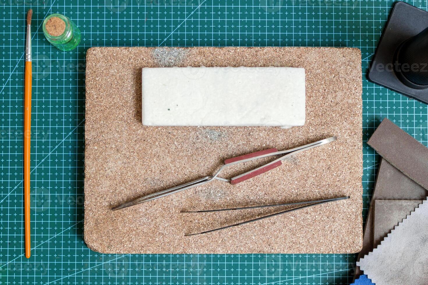 Tools for crafting handmade jewelry on green cutting mat - tweezers, foam block and sandpaper. photo