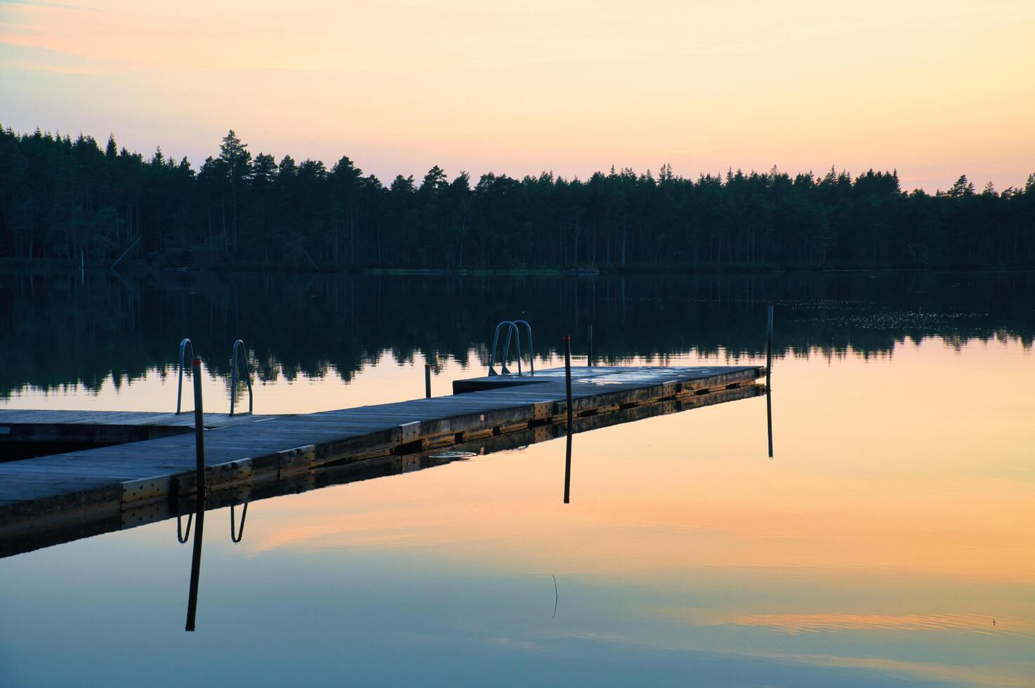 Wooden jetty at sunset on a Swedish lake. Sunset reflected in the water photo
