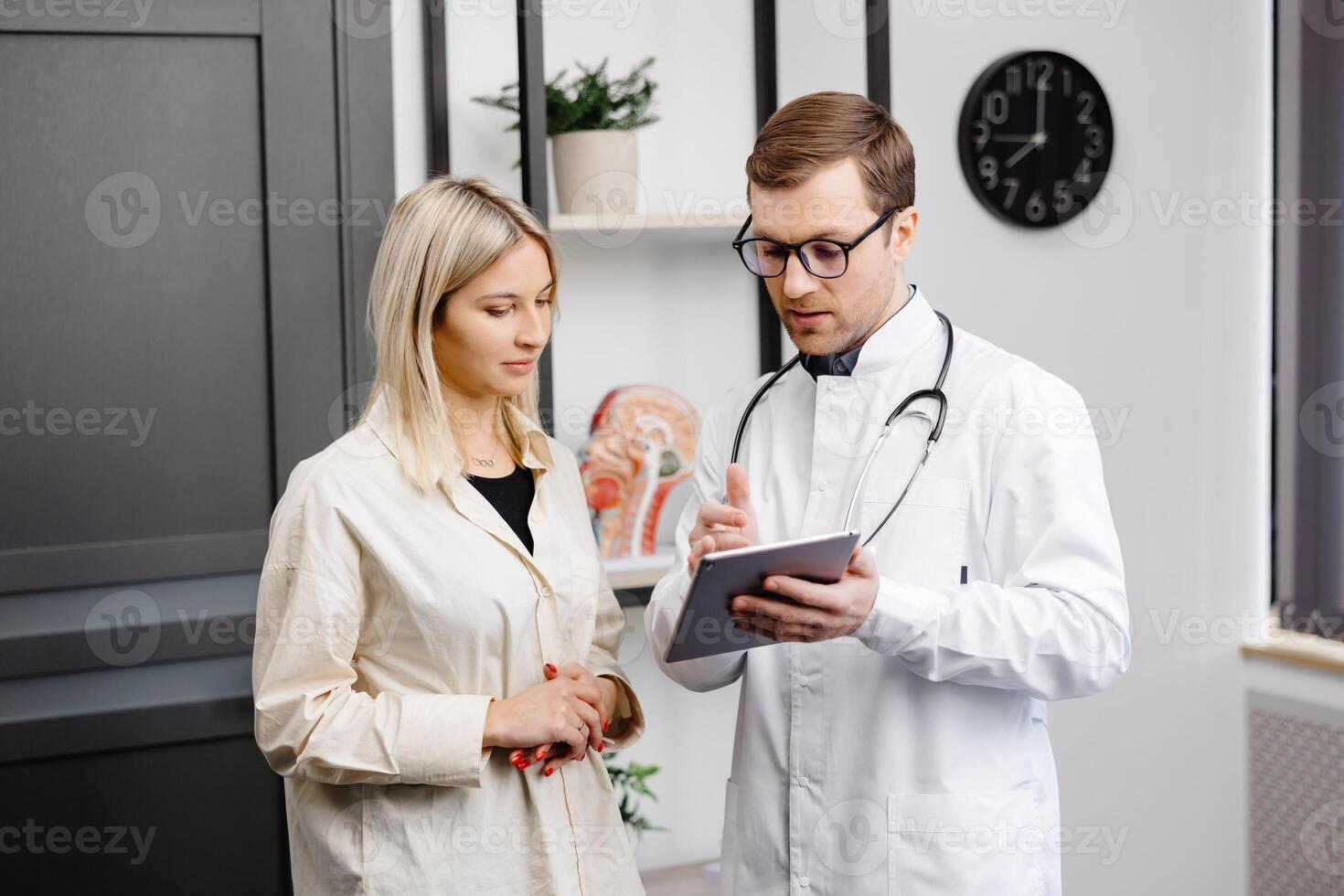 Happy man doctor showing tablet woman patient in clinic office interior. Health care, visit to family therapist, treatment of illness and medical help photo