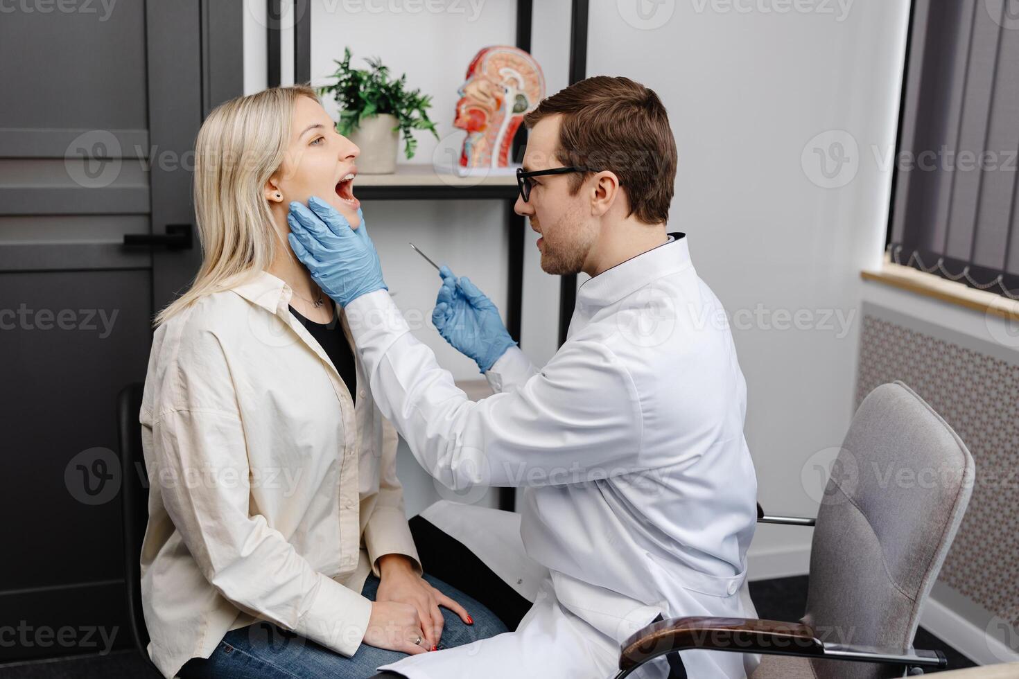 Doctor using inspection spatula to examine patient throat. ENT doctor doing throat exam of a woman. Patient opened her mouth to throat check-up photo