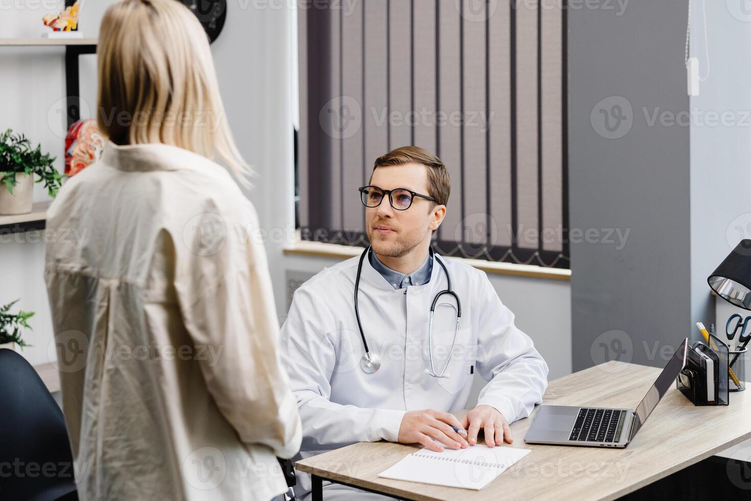 A young attractive doctor is having a consultation in his office. The doctor gives recommendations to his patient while sitting at the workplace photo