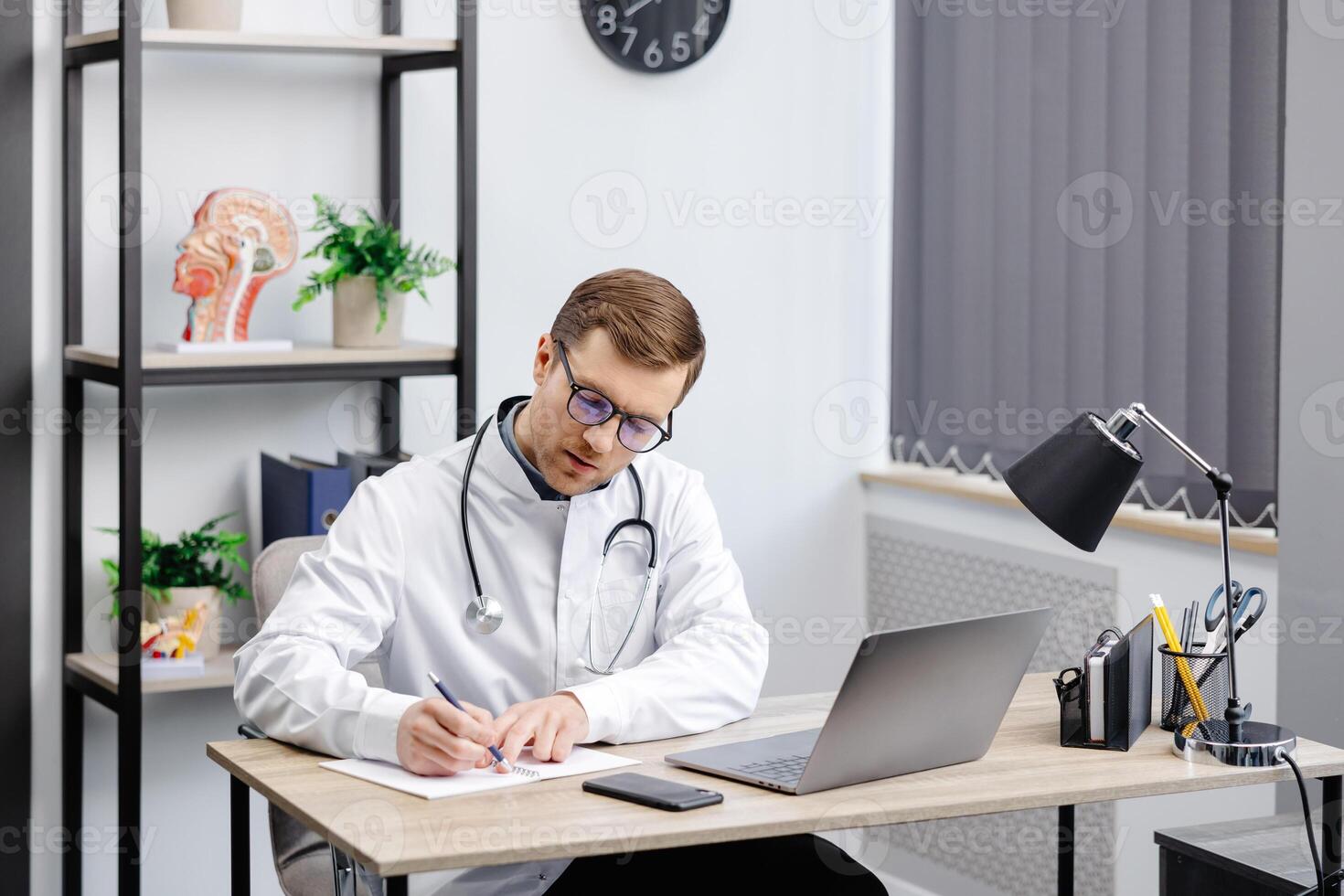 Doctor man sitting at the desk at his working place and working on laptop. Perfect medical service in clinic. Happy future of medicine and healthcare photo