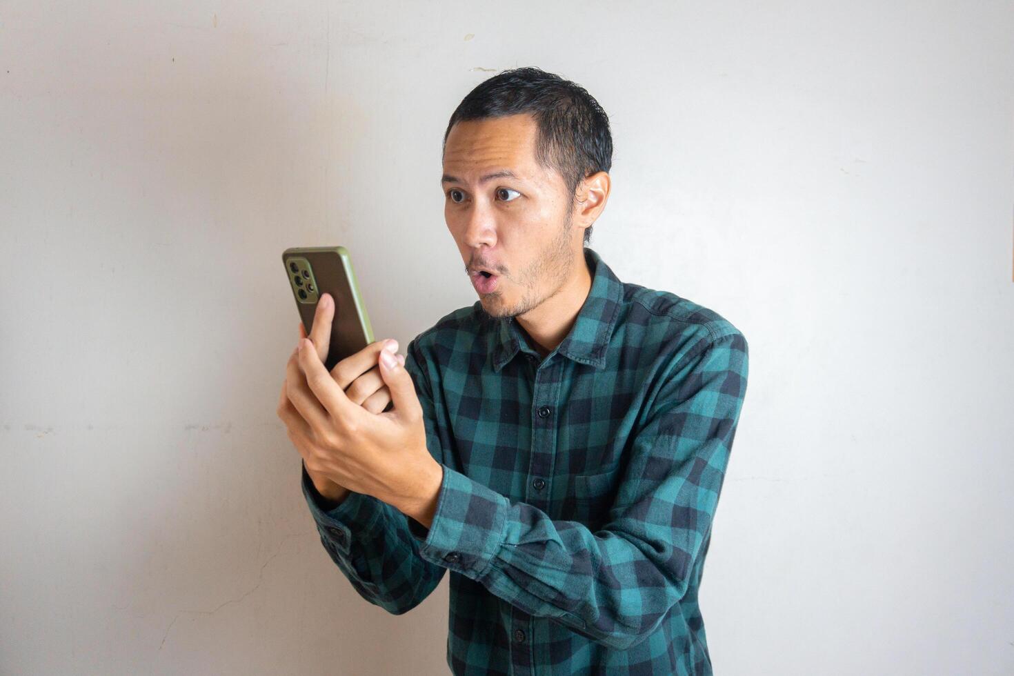 Young men wearing green flannel is shock by his smartphone on isolated white background photo