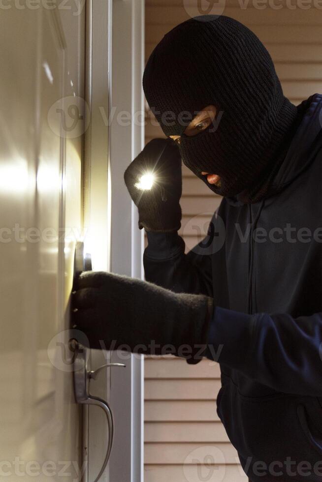 Masked burglar picking lock and entering house at night photo