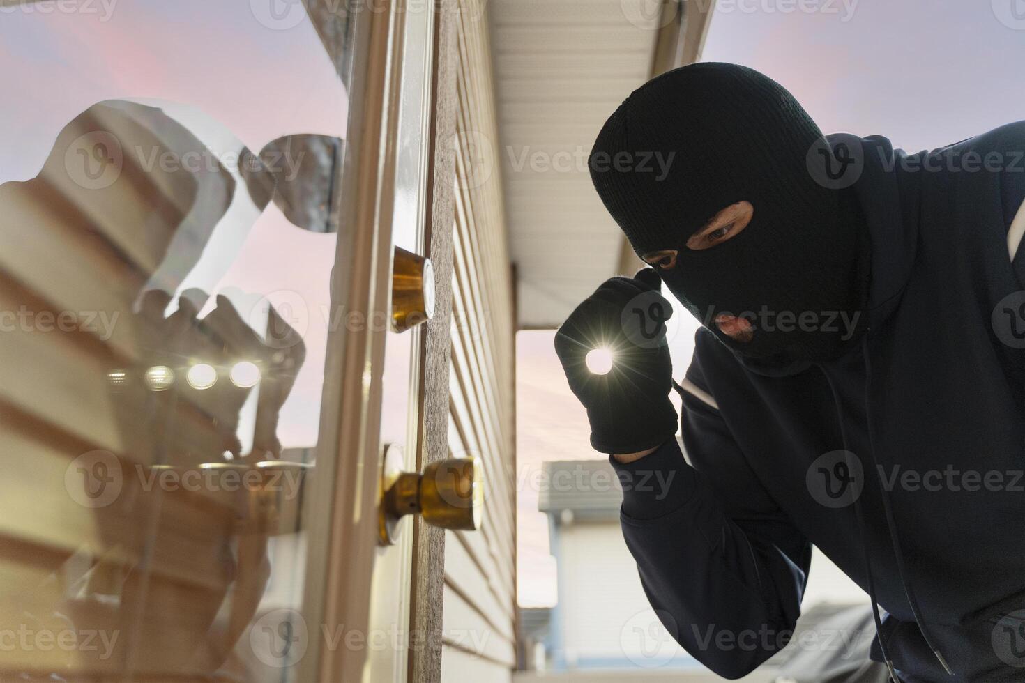 Masked burglar breaking into house at night using flashlight photo