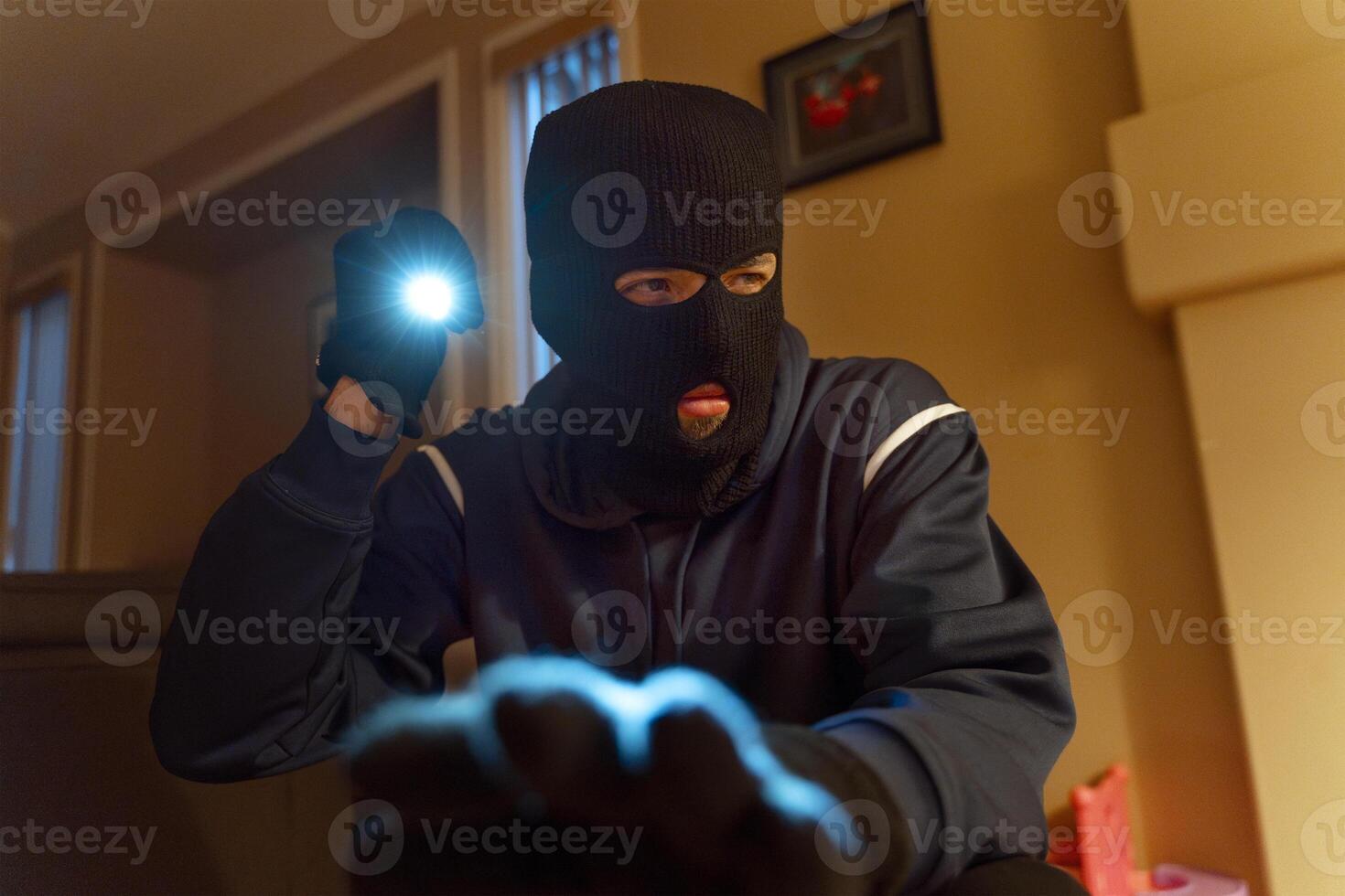 Masked burglar searching for valuables in living room photo