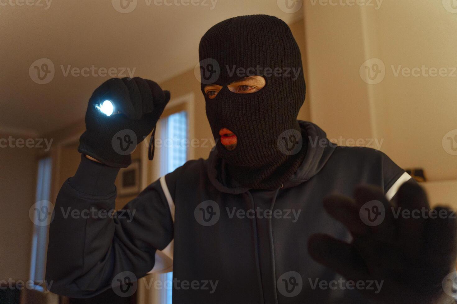 Masked burglar searching home at night using flashlight photo