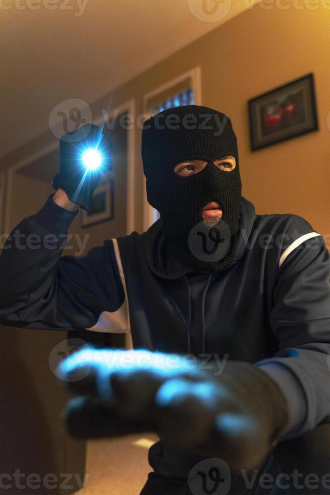 Masked burglar searching house at night with flashlight photo