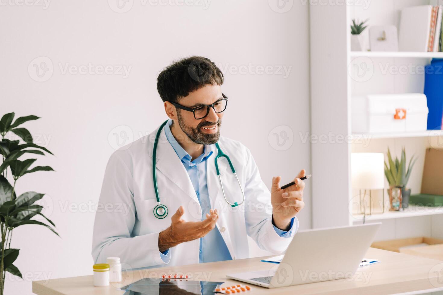 Attractive doctor wearing white coat using laptop having call, online consultation, explaining photo