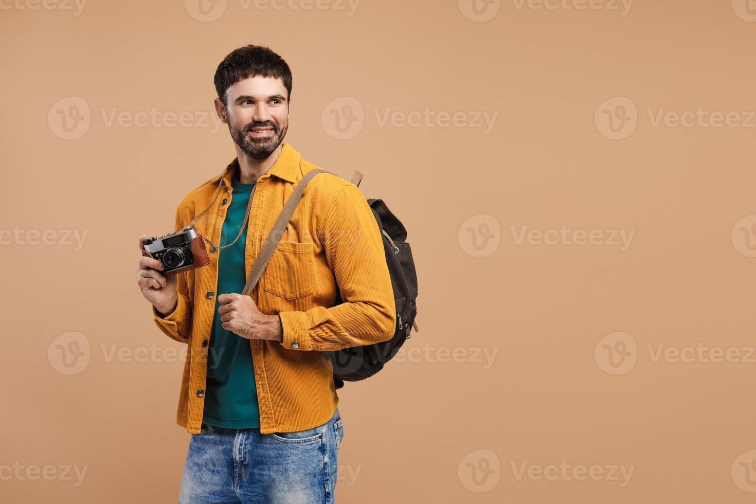 Portrait of smiling, handsome bearded man hipster holding backpack and camera traveling looking away photo