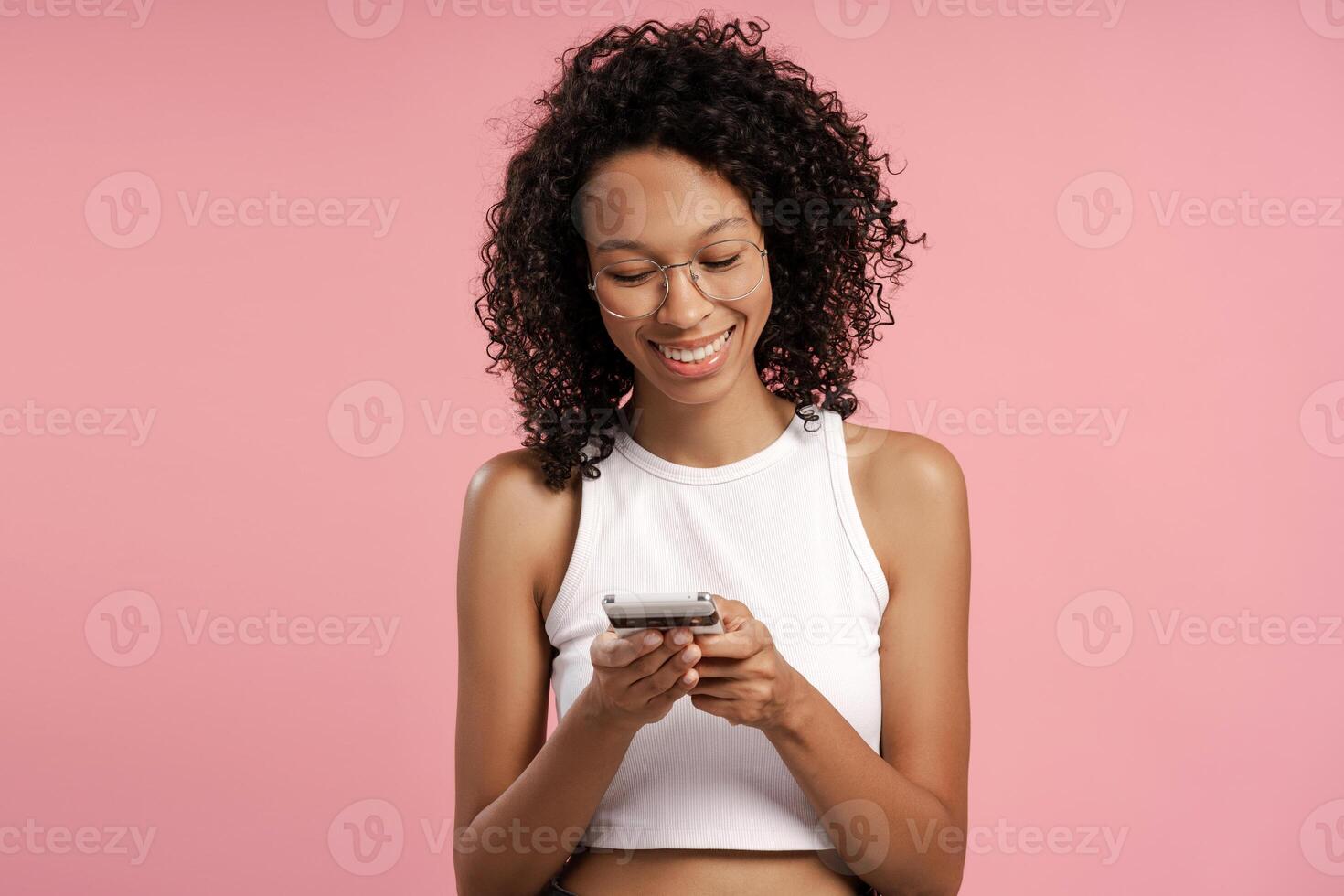 Smiling African American woman typing on mobile phone isolated on pink background photo