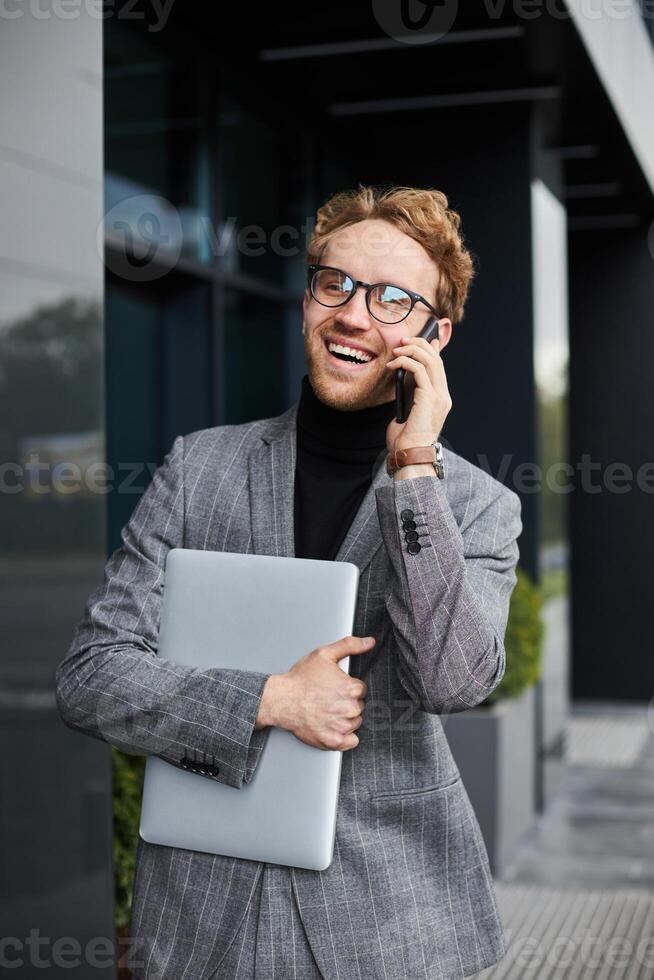 Businessman smiling while talking on phone and holding laptop photo