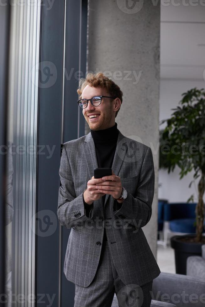 Businessman using smartphone and smiling by the window in office photo