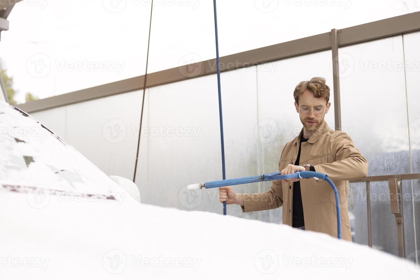 Man washing his car with soap and water in a self service car wash photo