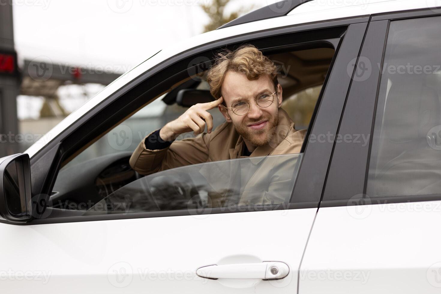 Skeptical driver pointing at his head while sitting in car photo