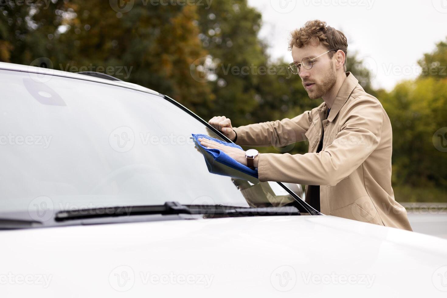 Young businessman cleaning windshield of his modern car in the street photo