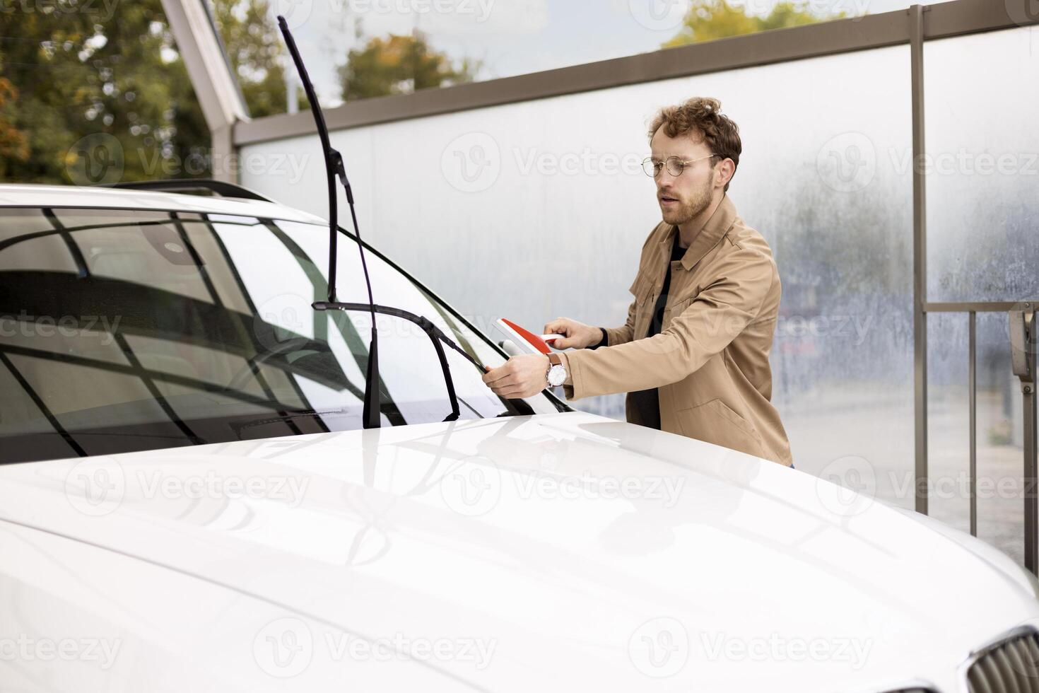 Young man cleaning windshield wipers of white car photo