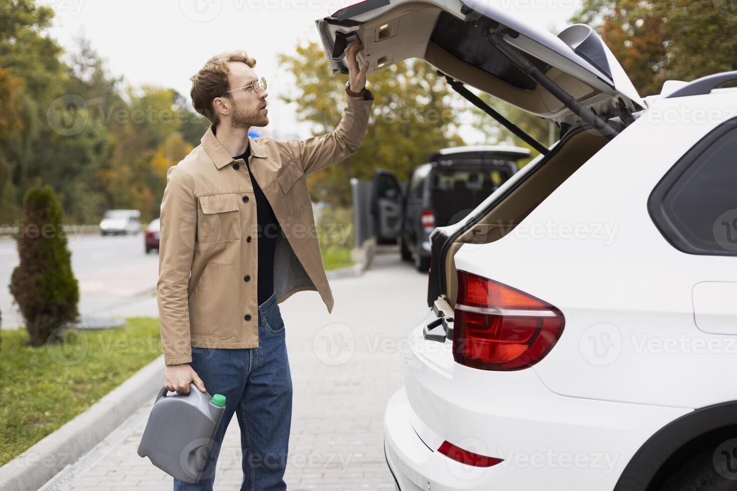 Stylish man holding engine oil checking his trunk before leaving for a road trip photo