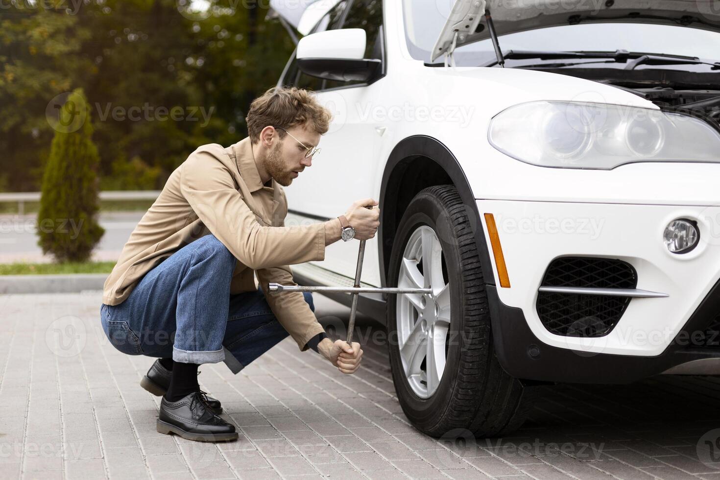 Young stylish man changing flat tire on his car using wrench outdoors photo