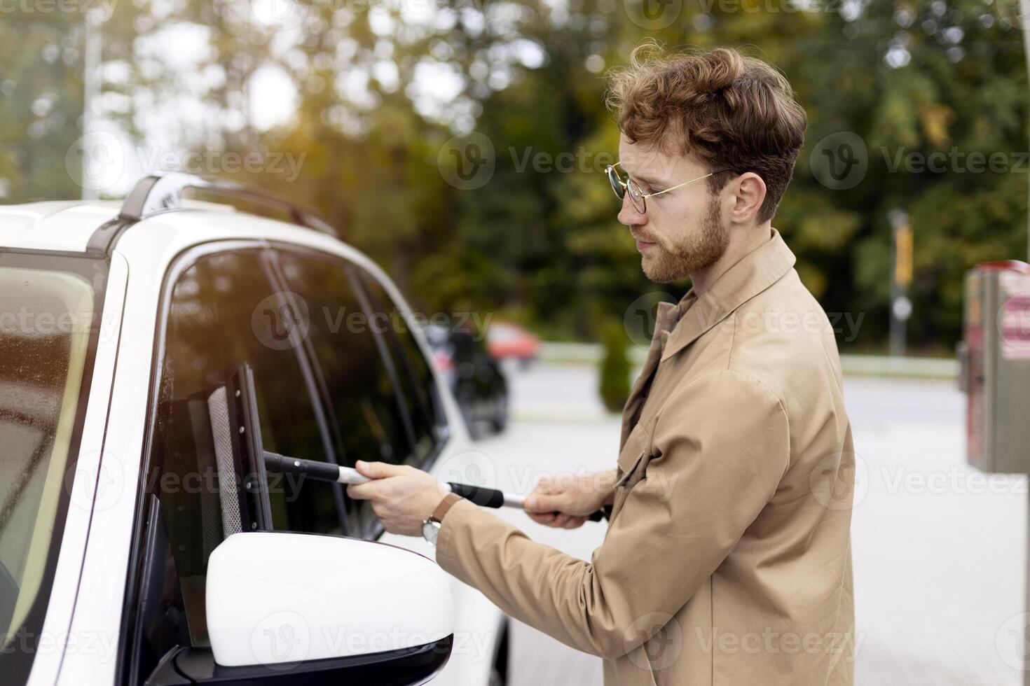 Young businessman cleaning his car with squeegee at self service car wash photo
