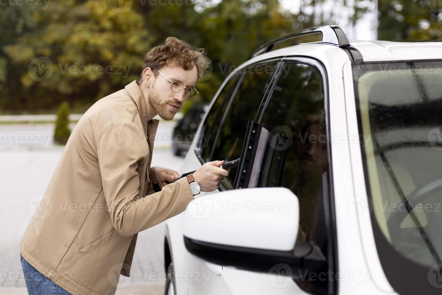 Man cleaning car window with squeegee after washing photo