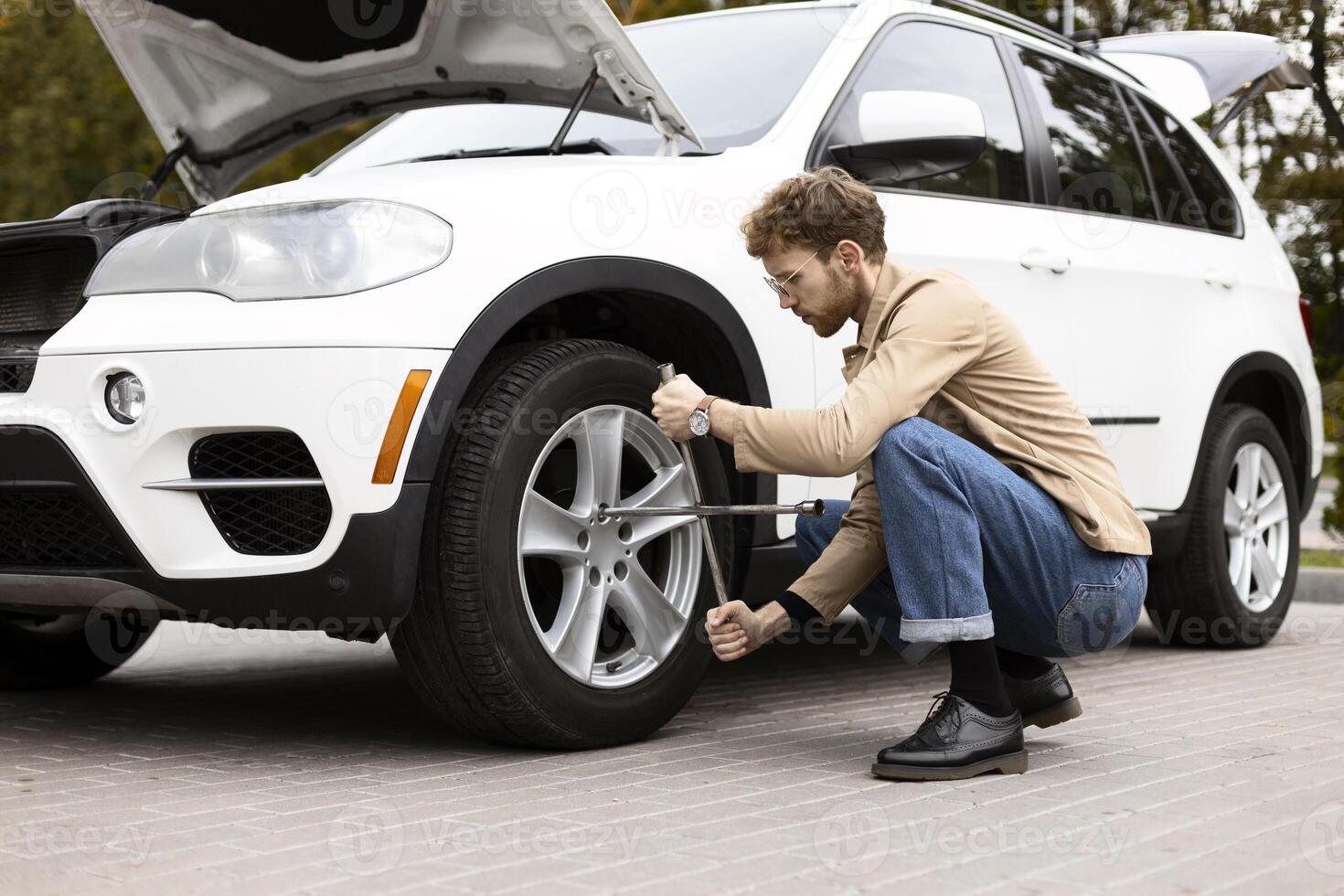 Young stylish man changing flat tire on modern suv photo